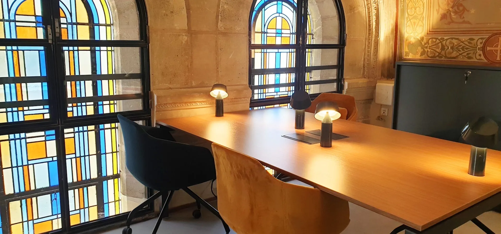 Bureau sous un vitrail bleu et jaune, éclairé par des lampes de table